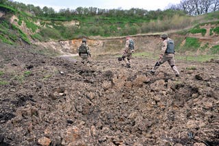 Deminers of Ukrainian Emergency Service walk past a crater following the explosion of anti-tank mines and other explosive materials, found in the town of Bucha